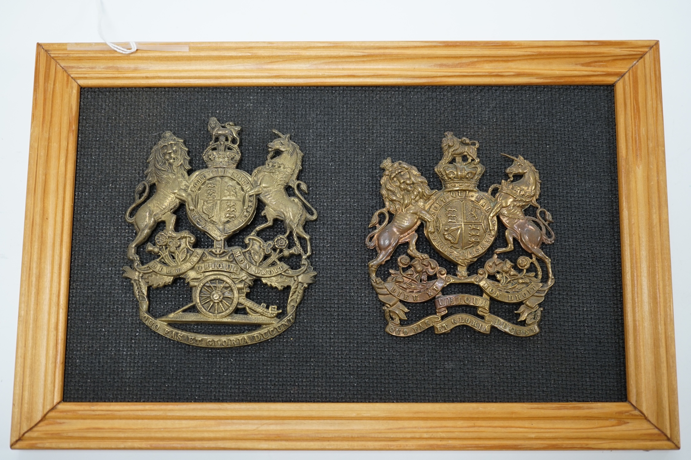 Two Royal Artillery brass helmet plates, one with three lugs and the other with two lugs, loosely mounted onto a backing board. Condition fair to good, top lug missing to one